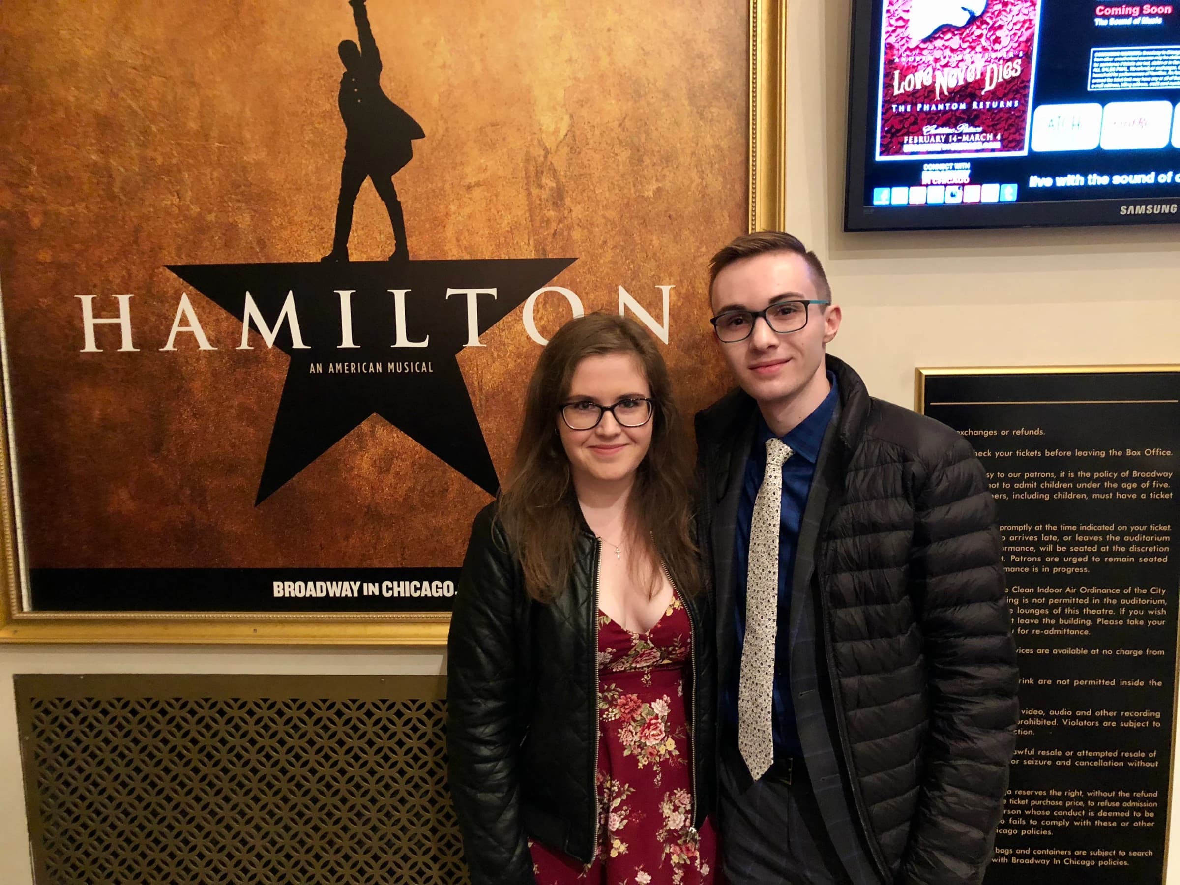 Rachel and Reid dressed up in front of a Hamilton poster in Chicago